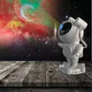 White galaxy astronaut light projector casting vibrant purple and blue nebula star patterns across a dark bedroom ceiling.
