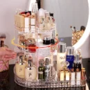 Transparent acrylic 360-degree rotating make up organizer filled with skincare bottles and lipsticks on a marble dressing table.