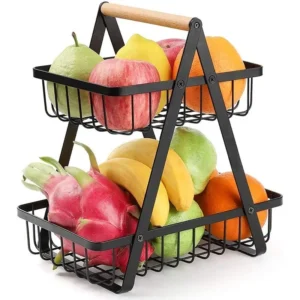 Minimalist matte black 2-tier metal kitchen basket filled with fresh red apples and green vegetables on a white marble countertop.