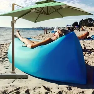 Bright orange inflatable camping mattress couch sitting on a sandy beach during a sunny afternoon.