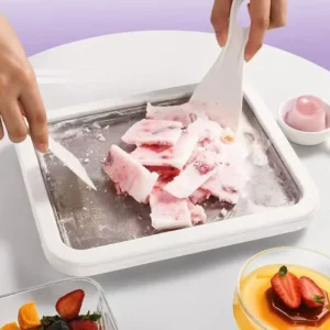 Bright blue rectangular rolled ice cream maker pan with two plastic scrapers rolling up fresh strawberry ice cream on a kitchen table.