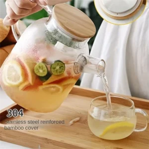 Clear glass kettle teapot filled with boiling fruit tea and fresh lemon slices sitting on a kitchen stovetop.