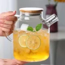 Clear glass kettle teapot filled with boiling fruit tea and fresh lemon slices sitting on a kitchen stovetop.
