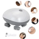 Pure white electric cat massager body tool gently kneading the head of a relaxed gray tabby cat on a soft bed.