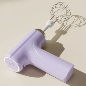 White cordless electric egg beater mixer standing upright on a clean kitchen counter next to a bowl of cake batter.