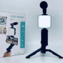 Desktop vlogging kit featuring a sturdy black tripod holder gripping a smartphone with an attached microphone and glowing LED light panel.